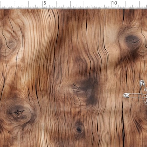 May include: A fabric featuring a realistic brown wood grain pattern with dark knots and vertical lines. A cluster of silver metal safety pins is attached to the right side. A ruler along the top and left edges shows measurements in cm and inches.