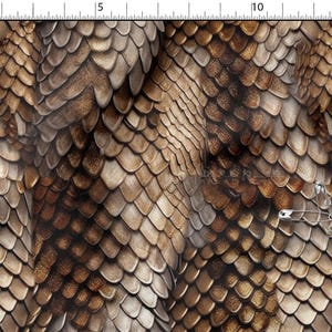 Op de afbeelding: Een close-up van een stof met een reptielschubbenpatroon in bruine en beige tinten. De overlappende schubben creëren een textuureffect. Verschillende zilveren veiligheidsspelden zijn op de stof bevestigd.