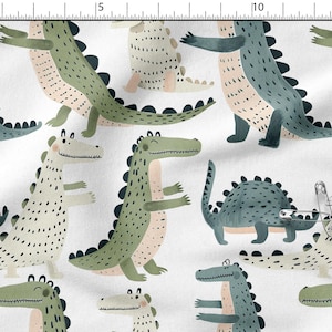 Pode incluir: Tecido branco com um padrão repetido de dinossauros de desenho animado. Os dinossauros são em tons de verde, azul e bege, com detalhes de pontos pretos. Ideal para roupas infantis ou decoração de berçário.
