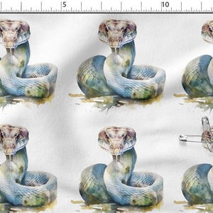 Puede incluir: Una tela blanca con una ilustración repetida en acuarela de una serpiente con escamas azules y verdes. Un imperdible de metal está sujeto a la tela cerca de la esquina inferior derecha. Una regla en los bordes muestra una escala en cm.