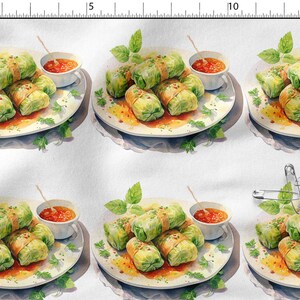 Peut inclure: Un tissu blanc avec un motif répétitif d'assiettes garnies de choux farcis, d'herbes vertes et de petits bols de sauce rouge. Une règle métallique est visible sur les bords supérieur et gauche, et des épingles à nourrice sont sur la droite.