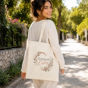 May include: A cream-colored canvas tote bag featuring a printed design of a circular wreath made of leaves and chain links. The text Rompiendo Ciclos is printed in the center of the wreath in a combination of serif and script fonts.