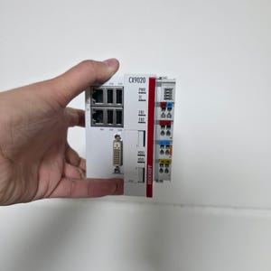 May include: A white Beckhoff CX9020 embedded PC controller featuring a red vertical stripe, multiple Ethernet ports, a DVI interface, and status indicator labels including PWR, TC, FB1, FB2, and HDD. The device includes a side-mounted terminal block.