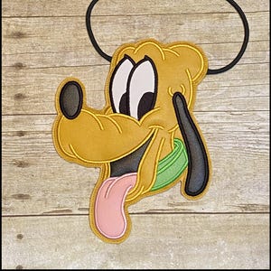 Könnte beinhalten: Ein Pluto-förmiges Schlüsselband mit gelbem, schwarzem und weißem Design, einer rosa Zunge und einem grünen Kragen. Das Schlüsselband hat eine schwarze Kordel und den Text "K's Kreations" oben.