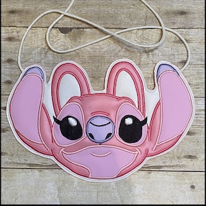 May include: Pink and white crossbody bag featuring a cartoon character face with large black eyes, a purple nose, and large ears. The bag has a white cord strap and the text "K's Kreations" at the top.
