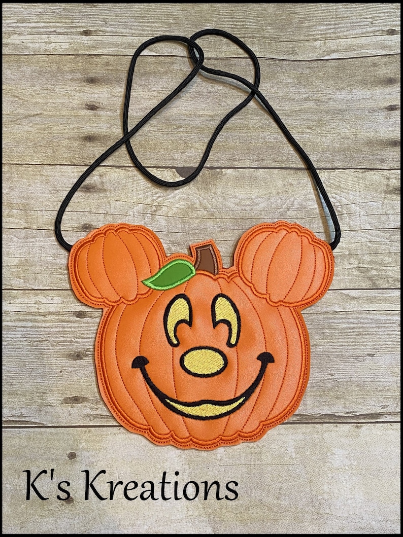 May include: Orange pumpkin-shaped crossbody bag with a black strap. The pumpkin has a smiling face, Mickey Mouse ears, and a green leaf. The text "K's Kreations" is at the bottom.