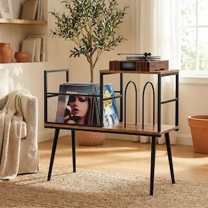 May include: A record player stand with a black metal frame and wood-tone shelves. The unit features a wire mesh storage bin for vinyl records on the left and two vertical metal dividers on the right side for organizing additional albums.