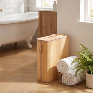 May include: A tall, rectangular laundry hamper made of light-colored bamboo slats with a matching lid and a single beige fabric handle on the side. The hamper features a flat top with a small handle and a vertical slatted design throughout the body.