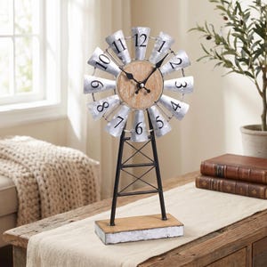 May include: A decorative windmill clock with a galvanized metal face and blades. The clock face is made of wood, and the numbers are black. The clock is mounted on a black metal stand with a wooden base. The clock measures approximately 18 inches tall.