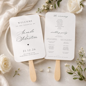 Può includere: Due ventagli bianchi per il programma di nozze con angoli arrotondati e manici in legno. Il ventaglio a sinistra riporta "WELCOME TO THE WEDDING OF Amanda & Sebastian 21.12.26 THE ASTOR MANOR CHARLESTON, SOUTH CAROLINA". Quello a destra elenca la cerimonia e gli sposi.