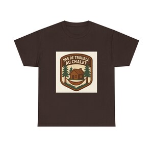 May include: A dark brown t-shirt with a graphic that reads "PAS DE TROUBLE AU CHALET". The graphic shows a cabin, trees, and a hammock within a shield design. The t-shirt is made of a soft, comfortable material.
