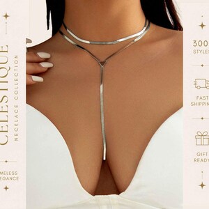 Puede incluir: Un collar en forma de Y de tono plateado con un diseño de cadena plana y flexible. La pieza consta de una sección superior estilo gargantilla conectada a una cadena larga y vertical que desciende desde un conector de enlace triangular central.