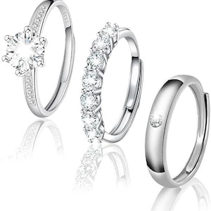 May include: A set of three silver-coloured rings featuring S925 markings. The first ring has a large central stone with pavé accents, the second features a row of six round stones, and the third is a smooth band with a single small embedded stone.
