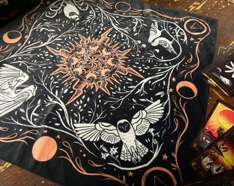 May include: Black cotton bandana with a white and orange design featuring a sun, birds, and an owl. The design is surrounded by a border of white leaves and branches.