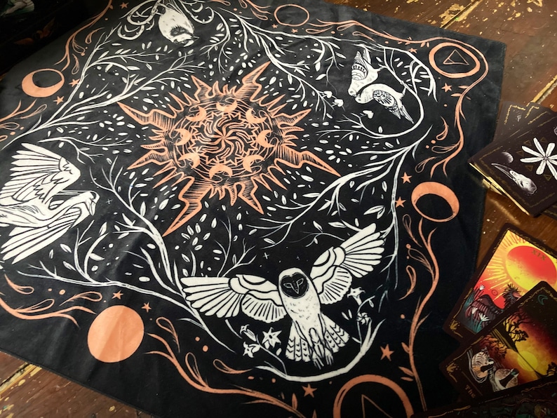 May include: Black cotton bandana with a white and orange design featuring a sun, birds, and an owl. The design is surrounded by a border of white leaves and branches.