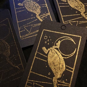May include: Four black cards with gold foil accents. Each card features a stylized illustration of a creature with a crescent moon in the background. The creature is depicted in a gold foil design.
