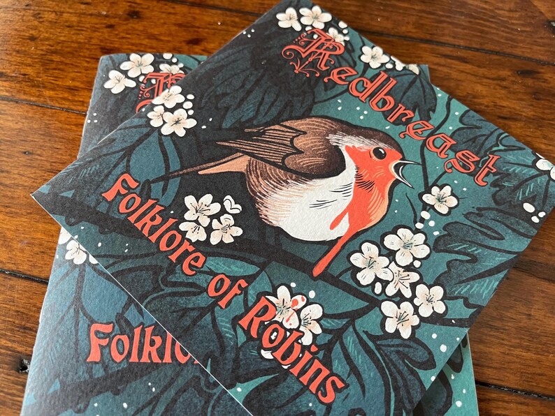 May include: Two book covers with a green background and white flowers. The top cover features a red robin with the text "Redbreast Folklore of Robins". The bottom cover has the text "Folklore of Robins" in red.