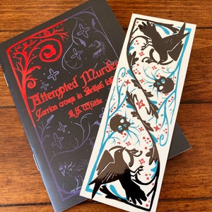 May include: A black book with a red title that reads "Attempted Murder: Carrion Crows in British Birds" by R.S. Whittle. The book is accompanied by a bookmark with a black and white illustration of birds and skulls on a white background with blue and red accents.
