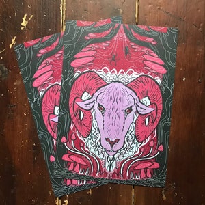 Puede incluir: Una cabeza de carnero rosa y blanca con grandes cuernos est&aacute; rodeada de setas rojas y blancas en un entorno de bosque oscuro. El fondo es rojo oscuro y negro con un dise&ntilde;o de telara&ntilde;a.