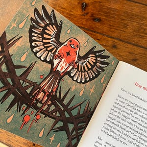 May include: A red robin perched on a thorny branch with blood dripping from its beak. The illustration is in a vintage style with a green background and gold stars. The text reads "How did the robin get its red breast?"