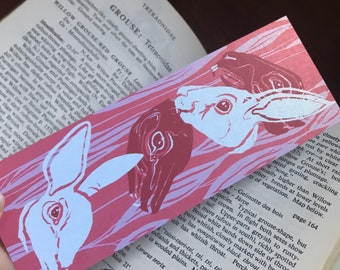 May include: A pink and white bookmark with a graphic design of three white rabbits with black eyes. The rabbits are in a stylized, almost abstract, design. The bookmark is printed with the text "Tetraonidae" and "Grouse: Tetraonidae".