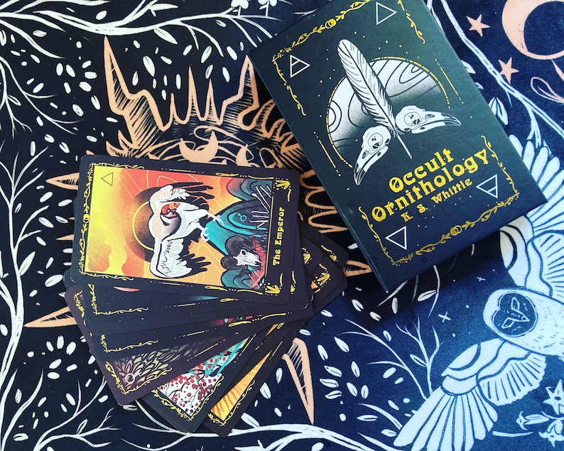 May include: A set of tarot cards with black backgrounds and colorful illustrations. The cards feature a bird theme and the text "Occult Ornithology K.S. Whittle".