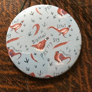May include: A round, blue mirror with a pattern of brown pheasants and the words "Strut", "Pretty Boy", "Babaaki", "So Handsome", and "Pre".
