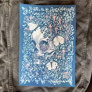 May include: A blue and white print of a skull surrounded by flowers and butterflies. The print is signed "Katie Whitlock".