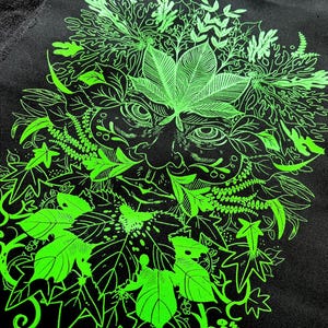 May include: A black fabric patch with a neon green depiction of the Green Man. The design shows a face surrounded by leaves and foliage, with detailed line work. The patch is likely for clothing or accessories.