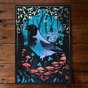 Puede incluir: Un cuervo azul y negro con un pico amarillo posado en un entorno de bosque. El cuervo est&aacute; rodeado de hojas verdes y setas rosas. El fondo es azul oscuro con detalles dorados.