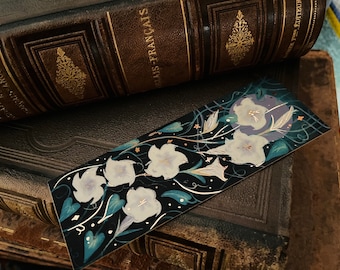 May include: A black bookmark with a floral design featuring white flowers and gold accents on a dark blue background.