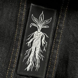 Op de afbeelding: Zwart-wit geborduurde patch van een humanoïde figuur met een plant die uit zijn hoofd groeit en wortels als benen.
