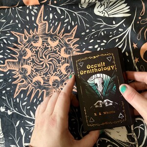 May include: A black and gold deck of cards called "Occult Ornithology" by K.S. Whittle. The cards feature a black and white illustration of a bird skull with a teal background.