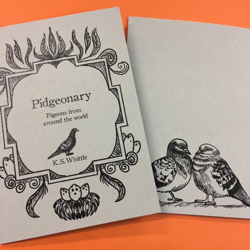 以下が含まれることがあります： 2冊の開いた小冊子。鳩のイラストが描かれています。1冊は「Pidgeonary」というタイトルで、副題は「Pigeons from around the world」、鳩の絵が描かれています。もう1冊には2羽の鳩のイラストが描かれています。