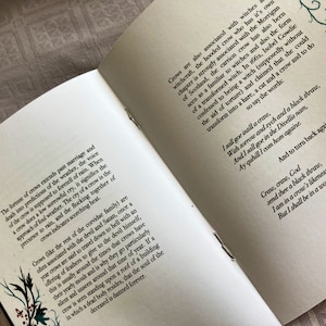 May include: Open book with white pages and black text. The text discusses the folklore and symbolism of crows. The book is open to a page with the text "I sall goe intill a craw, With sorrow and sych and a black thraw, And I sall goe in the Divellis nam, Ay quhill I com hom againe. And to turn back again:"