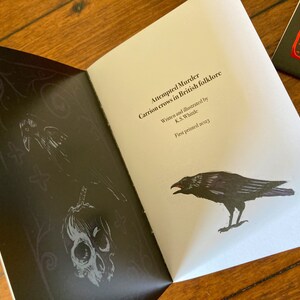 May include: A black and white illustration of a crow with a skull and crossbones on a black background. The text on the page reads "Attempted Murder Carrion crows in British folklore Written and illustrated by K.S. Whitle First printed 2023".