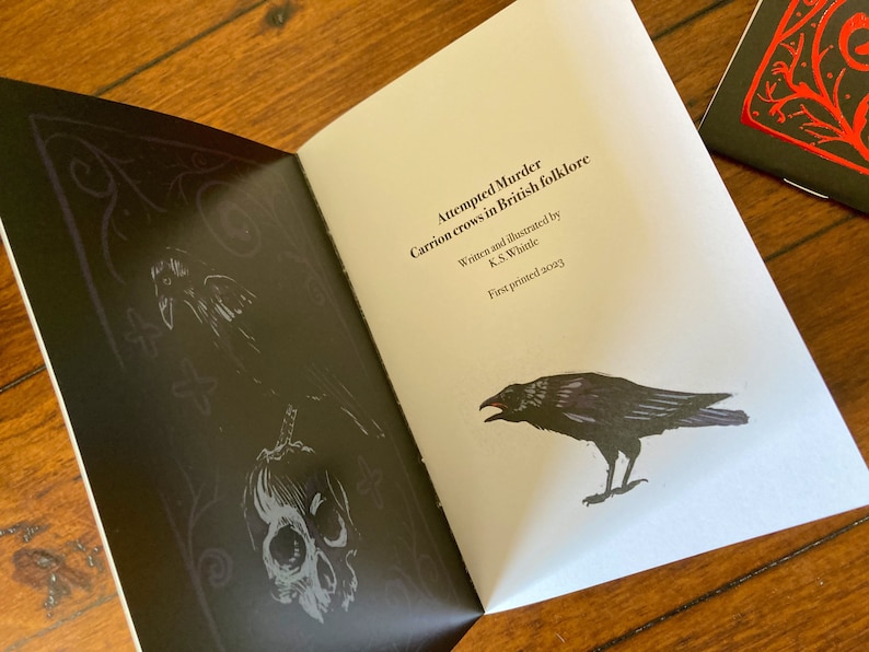 May include: A black and white illustration of a crow with a skull and crossbones on a black background. The text on the page reads "Attempted Murder Carrion crows in British folklore Written and illustrated by K.S. Whitle First printed 2023".