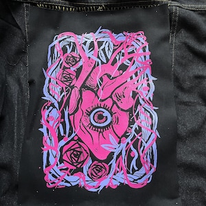 May include: A pink heart with an eye in the centre, surrounded by blue and pink vines and roses. The heart is on a black background.