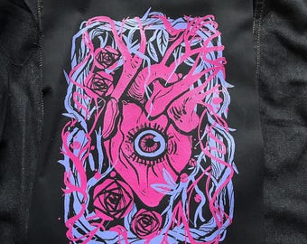 Könnte beinhalten: Ein pinkfarbenes Herz mit einem Auge in der Mitte, umgeben von blauen und pinkfarbenen Ranken und Rosen. Das Herz befindet sich auf einem schwarzen Hintergrund.