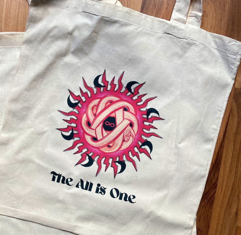 May include: A white tote bag with a pink and black sun design and the text "The All is One".