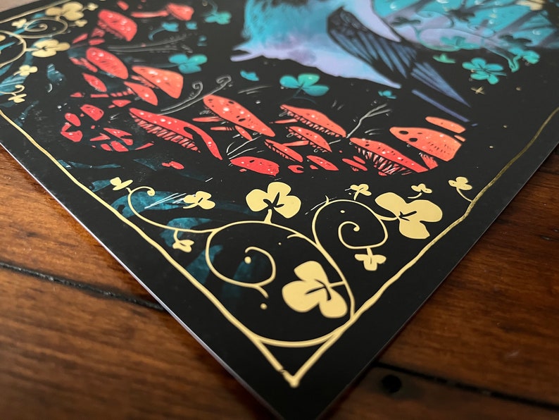 Puede incluir: Una tarjeta negra con un borde dorado y una ilustraci&oacute;n caprichosa de un p&aacute;jaro azul con las alas extendidas, rodeado de setas rojas y naranjas y tr&eacute;boles dorados sobre un fondo azul oscuro.