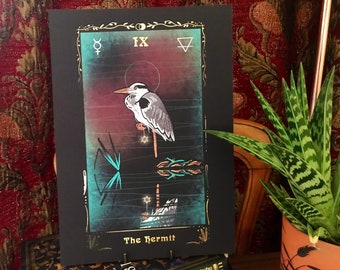 Op de afbeelding: De tarotkaart De Kluizenaar toont een grijze reiger die op een tak zit met een ster aan de top. De kaart is geplaatst tegen een donkere achtergrond met een verloop van rood, paars en blauw. Het kaartnummer IX en het symbool voor de planeet Mercurius bevinden zich in de linkerbovenhoek. De kaart is omlijst met goud met een bloemmotief.