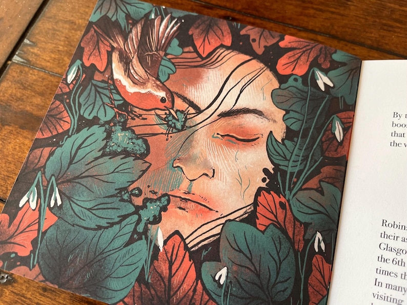 May include: A close-up of a book cover featuring a woman's face surrounded by green and red leaves, with a small bird perched on a branch. The woman's eyes are closed and she appears to be sleeping. The text on the page reads "By boo that the v Robin their as Glasgo the 6th times th In many visiting"