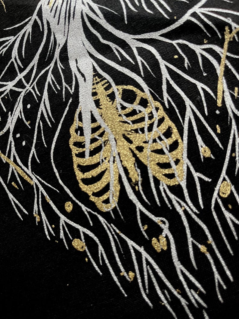 May include: A black fabric background with a white and gold design. The design features a rib cage with gold glitter and white branches.