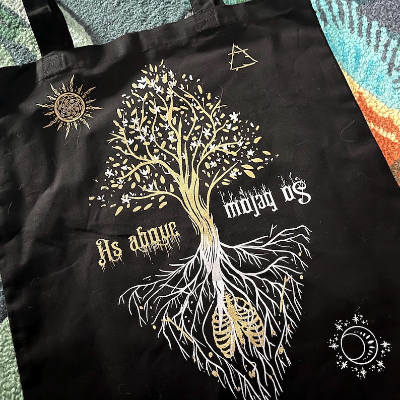 May include: Black tote bag with a white and gold design of a tree with roots and the text "As above so below".