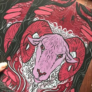 Puede incluir: Una cabeza de carnero rosa con grandes cuernos rojos est&aacute; rodeada de setas rojas y blancas sobre un fondo negro. Los ojos del carnero son rojos y el fondo es oscuro con l&iacute;neas blancas.