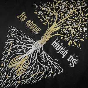 May include: A black fabric with a gold and white tree design. The tree has a white skeletal ribcage at its roots and the text "Its above" and "on below us" is written on the fabric.