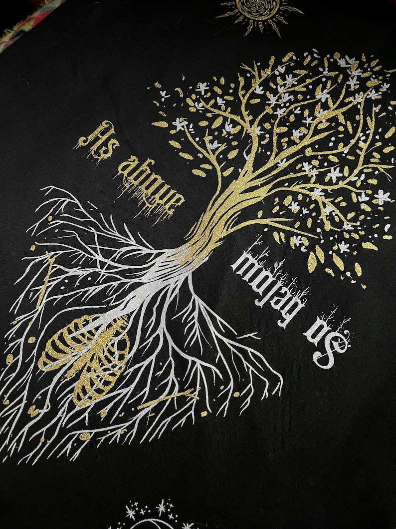 May include: A black fabric with a gold and white tree design. The tree has a white skeletal ribcage at its roots and the text "Its above" and "on below us" is written on the fabric.