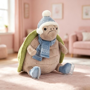 May include: A plush turtle toy featuring a tan body, a green shell, and a blue winter outfit consisting of a knit hat with a white pom-pom and a matching scarf. The turtle wears blue ice skates with silver blades on its feet, sitting upright.