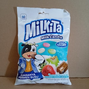 Może przedstawiać: Biała plastikowa torebka z mieszanymi cukierkami mlecznymi Milkita, przedstawiająca maskotkę krowy, świeżą truskawkę, kawałek melona i kostkę czekolady. Opakowanie zawiera napisy Milkita, High Calcium oraz Juaranya Permen Susu.